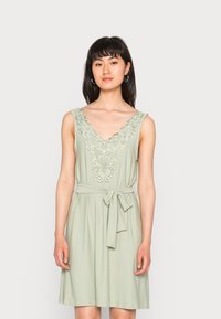 Vestido sem mangas verde menta com decote em V, bordado floral na gola e detalhe de cintura amarrada. Tecido suave com um corte relaxado.