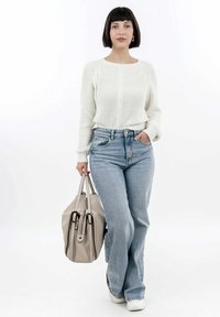 Pull en tricot blanc avec une texture côtelée, jean taille haute bleu clair et un sac à main beige. Modèle portant des baskets blanches, debout.