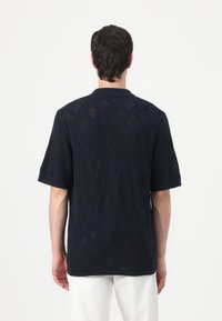 Tricou polo naval cu un model texturat în diamant, cu mâneci scurte și guler plat. Țesătura este respirabilă, având o calitate semi-transparentă.