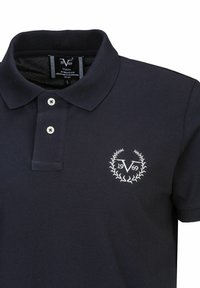 Marineblauwe polo gemaakt van gestructureerde stof, met een twee-knoopsluiting en een geborduurd logo met een laurierontwerp op de borst.
