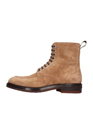 Stivaletto alla caviglia in camoscio beige con punta arrotondata, otto occhielli per i lacci e una robusta suola in pelle marrone. Dotato di linguetta posteriore per facilitarne la calzata.