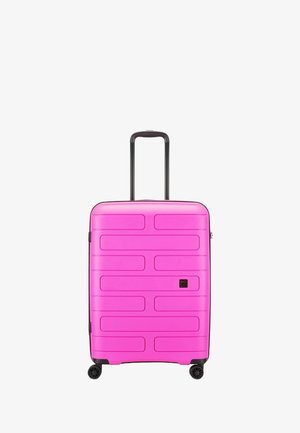 Valise rigide rose avec une surface texturée, une poignée rétractable et quatre roulettes noires. Présente des rainures horizontales et une finition lisse.