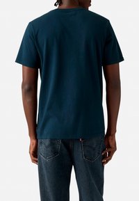T-shirt en coton bleu marine avec un col rond, à manches courtes et coupe décontractée, porté avec un jean en denim foncé doté de poches arrière.