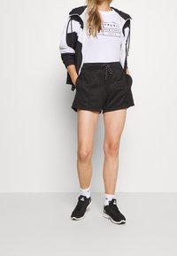 Černé šortky s elastickým pasem a šňůrkou, spárované s bílým tričkem s potiskem a černobílou bundou. Černé tenisky s bílou podrážkou.