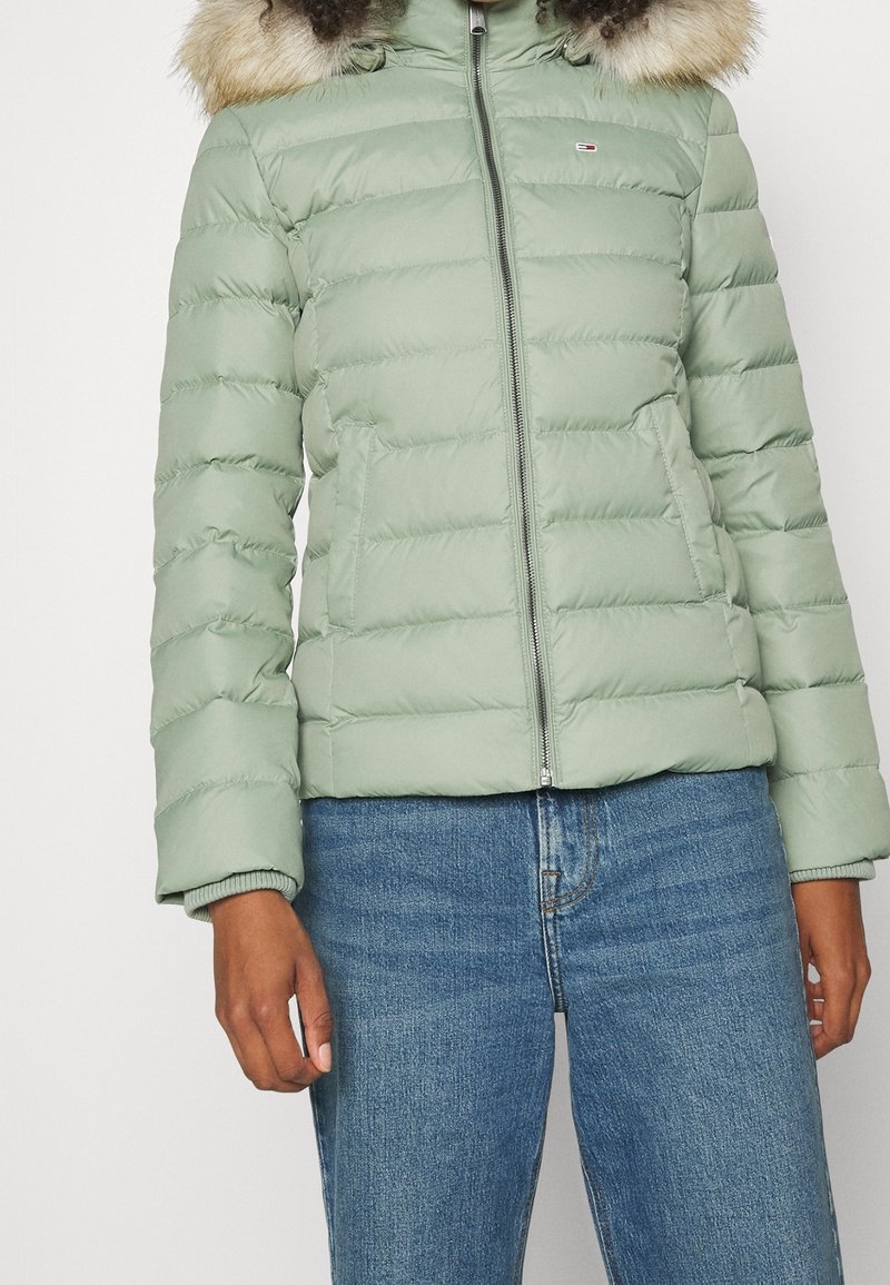 Jasnozielona kurtka puchowa z pikowanym wzorem, z zamkiem błyskawicznym i odpinanym kapturem obszytym futerkiem. Połączona z niebieskimi dżinsami.