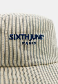 Kapelusz typu bucket w kolorze kremowym z niebieskimi pionowymi paskami. Posiada haftowane logo "SIXTH JUNE PARIS" w kolorze niebieskim. Teksturowany materiał z przeszyciami.