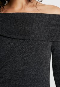 Haut ajusté, dégageant les épaules, en tissu maille gris foncé, présentant une texture côtelée et un large col. Matière douce et extensible.