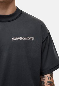 Zwarte oversized t-shirt met een ribbelige ronde hals. Voorzien van witte gestileerde tekst "GOODFORNOTHING" over de borst. Gemaakt van katoen.