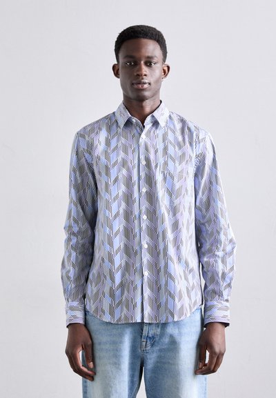 Camisa abotonada con un patrón geométrico azul y negro, de manga larga, con cuello, hecha de una tela ligera, combinada con jeans claros.