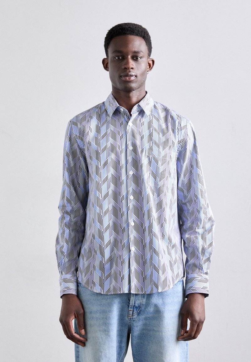 Camisa abotonada con un patrón geométrico azul y negro, de manga larga, con cuello, hecha de una tela ligera, combinada con jeans claros.