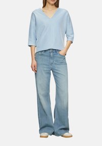 Lichtblauw gestreept v-hals shirt met driekwartmouwen, gecombineerd met ruime lichtblauwe denim jeans en beige sneakers.