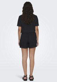 Completo nero a due pezzi composto da un top a maniche corte e pantaloni corti. I pantaloni corti hanno bordi scallop. Include sandali neri con cinturini.