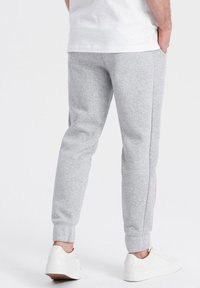 Grau Sweatpants aus weichem Material, mit schlankem Schnitt, elastischen Bündchen und kontrastierenden seitlichen Streifen in Orange. Getragen mit weißen Turnschuhen.
