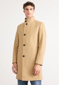 Palton dintr-un amestec de lână bej, cu guler înalt, design cu un singur rând de nasturi, șase nasturi negri și buzunare frontale. Textură netedă și croială ajustată.