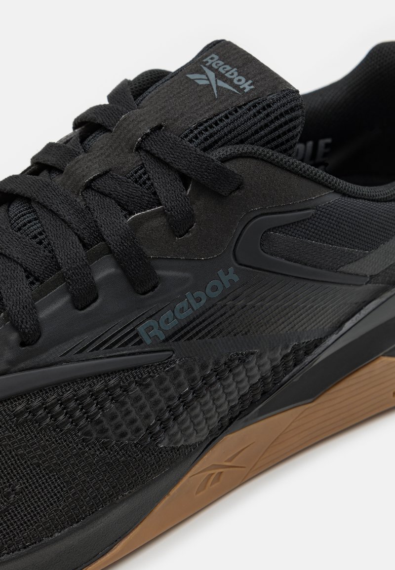 Baskets de sport noires en matériau mesh et caoutchouc, avec des accents texturés, des lacets et une semelle en gomme arborant le logo Reebok.