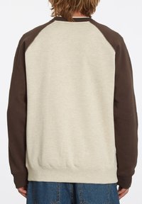 Sudadera de color beige claro con mangas raglán marrones, textura suave, puños y dobladillo acanalados. La vista trasera muestra un diseño minimalista y costuras.