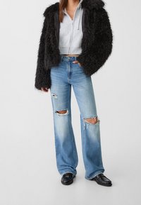 Musta pörröinen takki, harmaa lyhyt huppari ja vaaleansiniset leveälahkeiset farkut, joissa on kuluneet reiät polvissa. Asun viimeistelevät mustat loafersit.