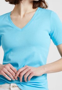 Vaaleansininen, hyvin istuva puuvillainen T-paita, jossa on V-mallinen kaula-aukko ja lyhyet hihat. Paita on sileä ja saumaton rakenteeltaan.