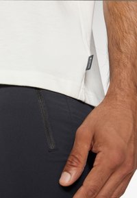 White cotton t-shirt with a black tag at the hem, paired with black athletic pants featuring a zippered pocket detail.