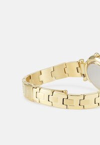 Goldfarbener Metallarmbanduhr mit rechteckigem Glieddesign, glatter Oberfläche, rundem Zifferblatt und Kronsymbol an der Position 2 Uhr.