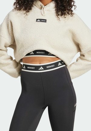 Kvinde iført off-white cropped fleece-hættetrøje og højtaljede sorte leggings med "Moon Boot" mærkede taljebånd og logoer.
