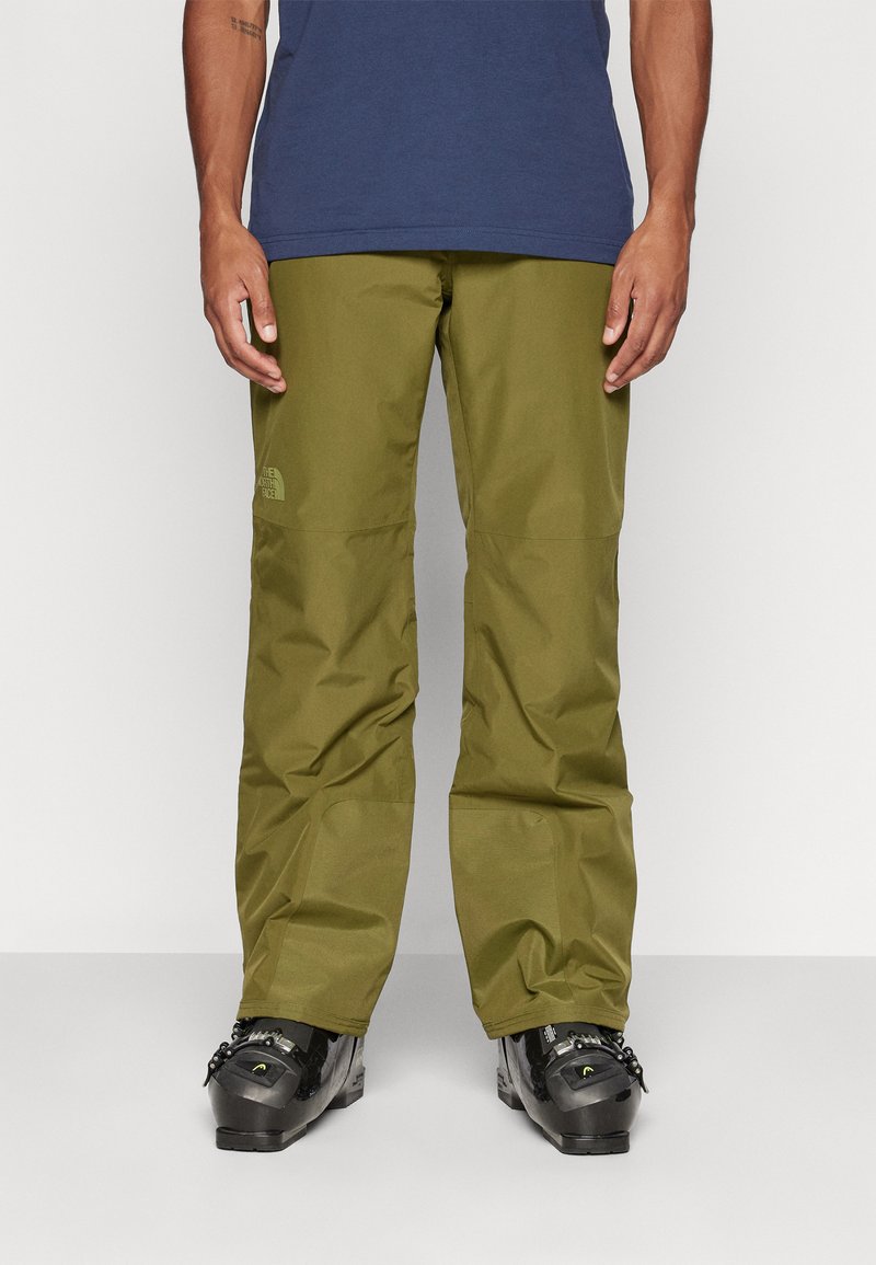 Olive green waterproof pants with a relaxed fit, featuring reinforced knees and the North Face logo on the left thigh, paired with black boots.
