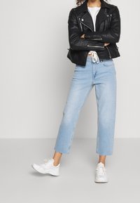 Svart läderbikerjacka, vit t-shirt, ljusblå korta jeans och vita sneakers. Nyckelfunktioner inkluderar dragkedjor och en avslappnad passform.