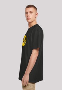 Black cotton t-shirt with a round neckline, short sleeves, and a large yellow graphic logo on the front. Casual fit.