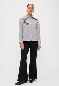 Striped button-up shirt in white and navy, featuring floral embroidery on the shoulders. Paired with black flared pants and flat shoes.
