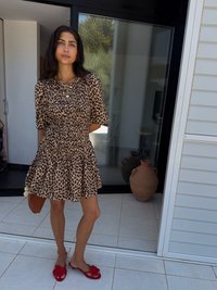 Leopardprint korte jurk met een gathered lijfje en een uitlopende rok. Draag het met rode sandalen met bloemaccenten en houd een bruine clutch.