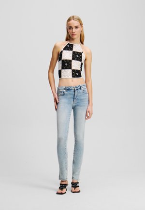 Gehaakte haltercrop-top in zwart, wit en beige met een ruitpatroon, gecombineerd met lichtblauwe skinny jeans en zwarte sandalen.