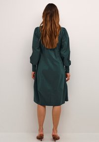 Dunkelgrünes, knielanges Kleid mit Puffärmeln, glatter Textur und taillierter Passform. Schlichte Gestaltung, keine sichtbaren Muster oder Verzierungen.