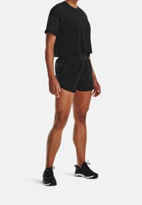 Svart träningsset bestående av en kortärmad cropped topp och matchande shorts. Materialet verkar lätt och har en slät textur. Svarta sneakers fulländar outfiten.