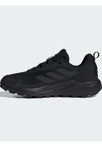 Des chaussures de sport noires en mesh et matériaux synthétiques, avec une semelle texturée, un bout renforcé et trois bandes diagonales sur le côté.