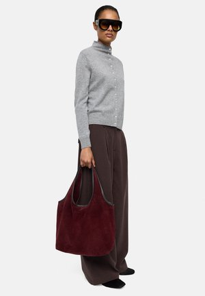 Szary dzianinowy kardigan z wysokim kołnierzem i guzikami, połączony z brązowymi spodniami o szerokich nogawkach. Ciemnobordowa torebka typu tote z zamszu z dwoma uchwytami.