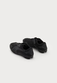 Zapatillas deportivas negras con un material texturizado, diseño redondeado y suelas de goma con clavos. Cuentan con una correa y un sutil detalle del logo.