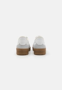 Vita sneakers med grå mockaaccenter, gummisula och vadderad krage. "Moschino"-logotyp präglad på hälen. Klassisk atletisk design.