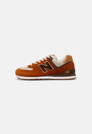 Brun og beige New Balance sneaker med ruskind og mesh overdel, hvide snørebånd og gummisål på en enkel lys baggrund.