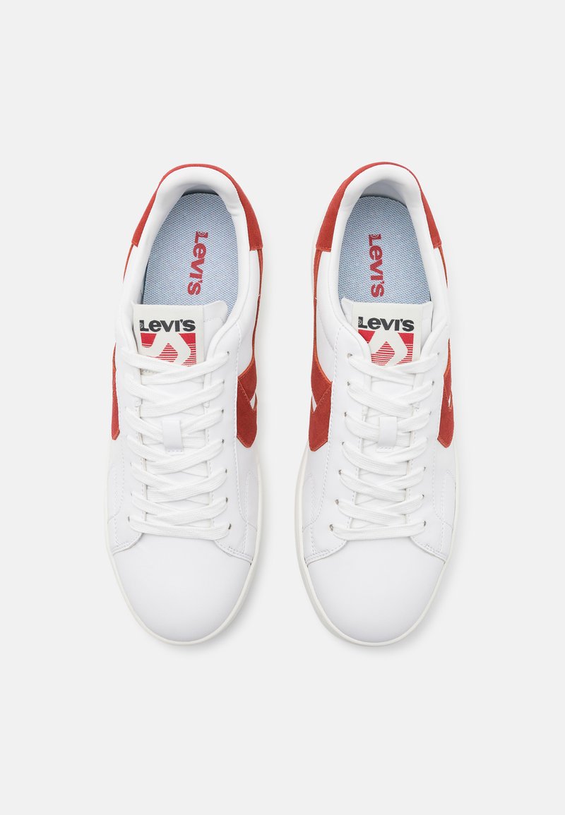 Baskets blanches avec des accents en daim rouge, dotées de lacets, d'une semelle texturée et d'une semelle intérieure bleue. Logo Levi's visible sur la languette.