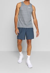Grey striped sleeveless tank top, blue shorts, white sneakers, and white socks; athletic fit, lightweight material, and logo accents.