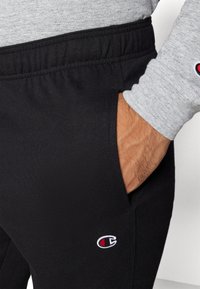 Sorte joggebukser med elastisk midje og sidelommer, med en liten brodert logo på venstre lår. Myk tekstur.