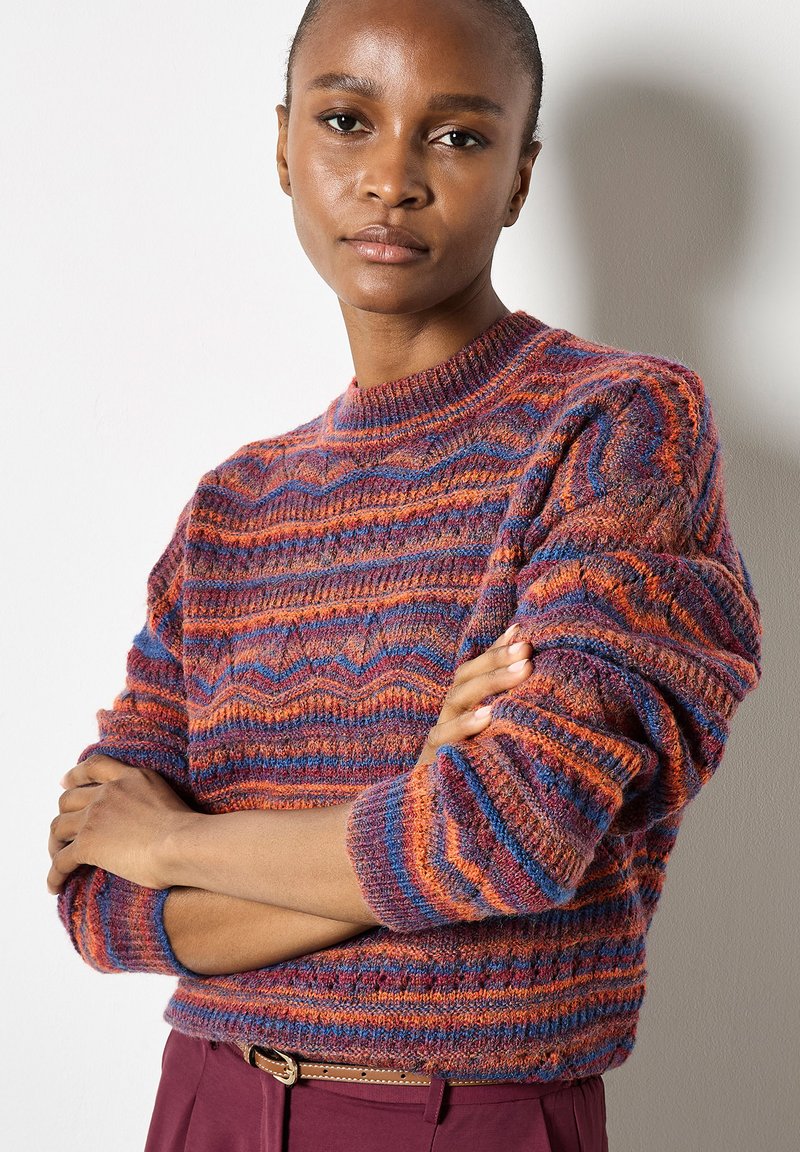 Knit sweater with a round neckline, featuring multicolored zigzag patterns in shades of orange, purple, and blue; textured wool material.