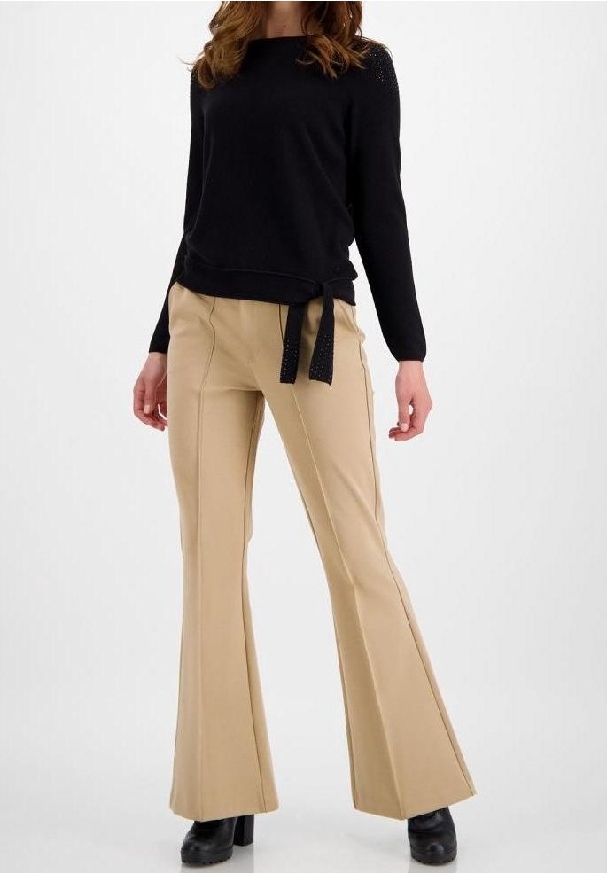 Suéter negro de manga larga con lazo lateral y detalle de malla. Pantalones acampanados color beige con acentos en las costuras. Botas de tobillo negras con plataforma.