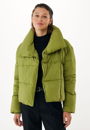 Grøn pufferjakke med høj krave, der har et quiltet design, frontlynlås og blød, glat tekstur. Båret over en mørk top.