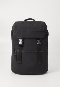 Zaino in nylon nero con cappuccio superiore, accessori in argento, tasca frontale con zip, spallacci imbottiti e regolabili, e logo del marchio impresso sulla parte anteriore inferiore.