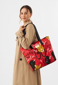 Rode totebag met zwarte handvatten, versierd met dierenmotieven en handgeschreven tekst in verschillende kleuren. Gemaakt van duurzaam materiaal met een glanzende afwerking.