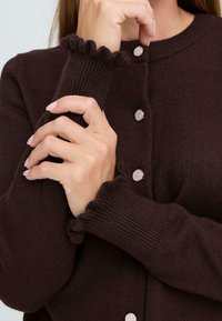 Brauner gerippten Cardigan mit rundem Halsausschnitt, Knopfverschlüssen und voluminösen Bündchen. Der Stoff wirkt weich und strukturiert.
