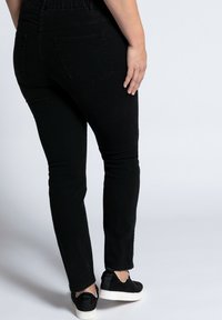 Černé džíny skinny s vysokým pasem, pěti kapsami a hladkou texturou, doplněné černými slip-on botami.
