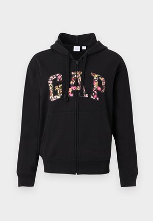 Μαύρο φούτερ με φερμουάρ, με μεγάλα γράμματα GAP γεμάτα με ροζ και κίτρινο λουλουδένιο μοτίβο στο μπροστινό μέρος, διαθέτει κορδόνια και μπροστινές τσέπες.