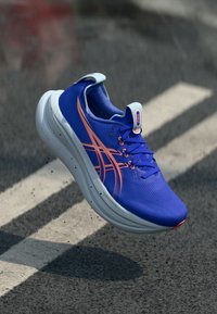 Niebieski but sportowy o smukłym designie, z gładką teksturowaną cholewką, kontrastowymi pomarańczowymi paskami i wyściełaną białą podeszwą.